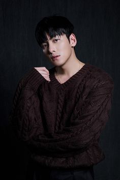 a young man with black hair wearing a brown sweater and posing for a studio photo