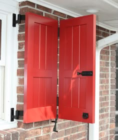 an open red door on the side of a brick building with white trim and black hardware