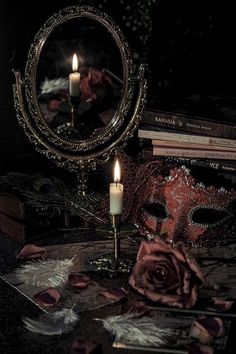 a candle is lit in front of a mirror on a table with books and masks