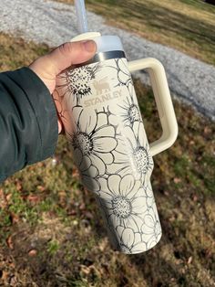 a hand holding a white and black flowered coffee cup in front of a grassy area