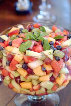 a glass bowl filled with fruit salad on top of a wooden table