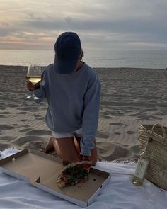 a person sitting on the beach with a glass of wine in their hand and half eaten pizza