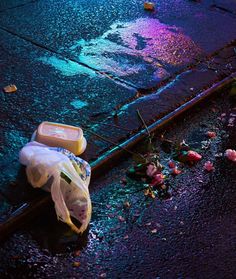 a trash can sitting on the side of a road next to flowers and plastic bags