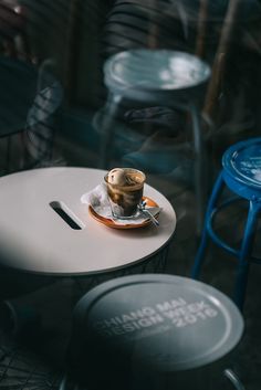 a cup of coffee sitting on top of a white plate next to two blue stools