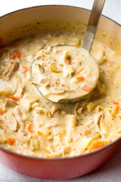 a ladle full of chicken noodle soup in a red pot