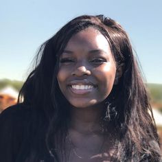 a close up of a person with long hair smiling and wearing a black shirt in front of cows