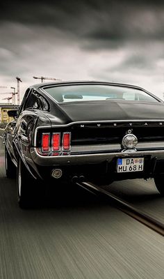 an old car driving down the road with dark clouds in the sky behind it,