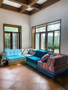 a living room filled with lots of furniture next to two large windows on top of a tiled floor