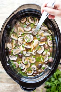 a spoon full of soup with mushrooms and parsley in the bowl, being held by someone's hand