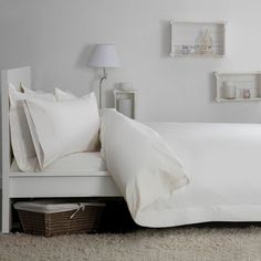 a bed with white sheets and pillows on top of it next to a night stand