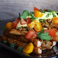 a black plate topped with tofu, tomatoes and green garnish on top of it