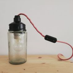 a glass jar with a red cord attached to it sitting on a wooden table next to a white wall