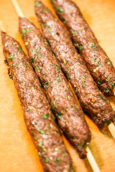 several skewers of meat sitting on top of a wooden cutting board with green sprinkles