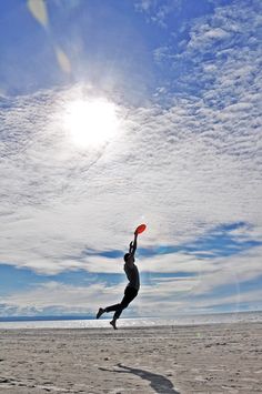 a person jumping up in the air to catch a frisbee at the beach