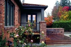 a brick house with steps leading up to the front door and patio area, surrounded by greenery