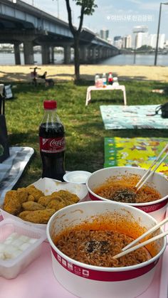 two bowls of noodles with chopsticks in front of a picnic table and water bottle