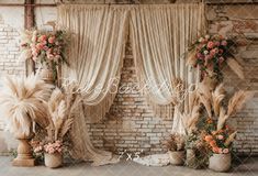 an arrangement of flowers and plants on display in front of a brick wall with drapes