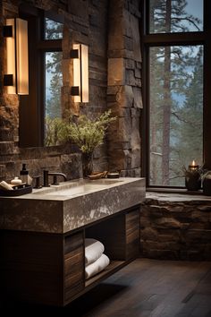 a bathroom with stone walls and flooring next to a large window overlooking the forest