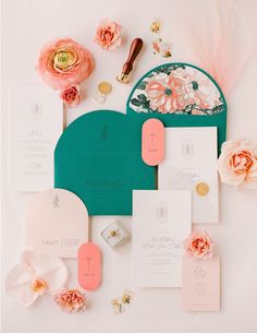 the wedding stationery is laid out on top of the table with pink flowers and green envelopes