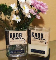 two jars with flowers in them sitting on a table next to a candle and some rocks