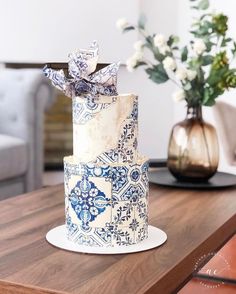 a blue and white cake sitting on top of a wooden table next to a vase with flowers