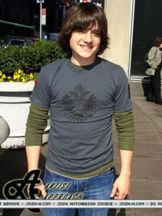 a young man standing in front of a building with his hands in his pockets and smiling at the camera