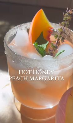 a close up of a drink in a glass with fruit on the rim and text that reads hot honey peach margarita