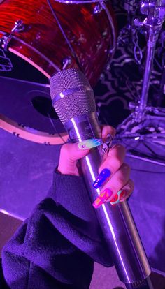 a woman holding a microphone in front of a drum set and purple lighting behind her