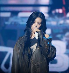 a woman with long black hair holding a microphone in her right hand and wearing a leather jacket