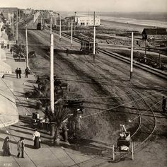 an old black and white photo of people walking on the side of a road near train tracks