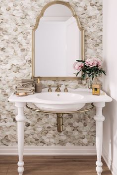 a white sink sitting under a mirror next to a vase with flowers on top of it