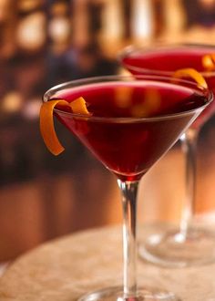 two martinis with orange peel garnish sit on a table