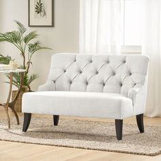 a white couch sitting on top of a wooden floor next to a table and potted plant