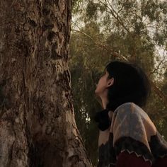 a woman standing in front of a tree looking up at the sky with her eyes closed