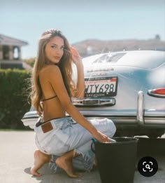 a beautiful young woman sitting on the back of a car next to a black suitcase