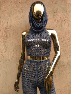 a mannequin is dressed in blue crochet and stands next to a wall