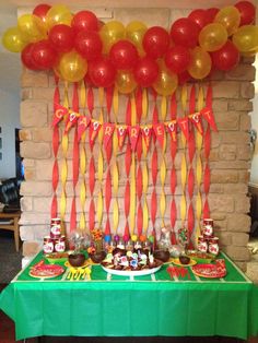 a green table topped with lots of balloons and desserts next to a brick wall