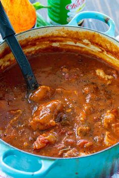 a blue pot filled with meat and sauce on top of a wooden table next to an orange napkin