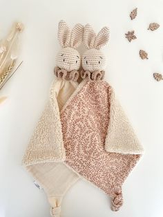 two knitted rabbits wrapped in a blanket next to dried flowers and feathers on a white surface