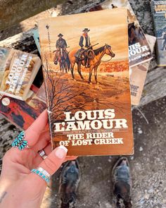 a person holding up a book about the rider of lost creek, with other books in the background