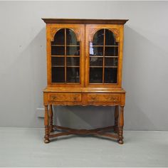 an old wooden china cabinet with glass doors on the top and bottom shelf, in front of a gray wall