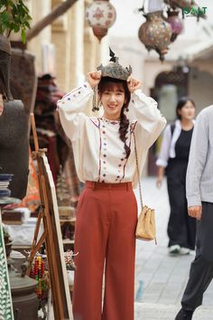 a woman is standing in the street with her hands on her head and wearing a hat