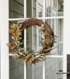 a wreath on the front door of a house with autumn leaves hanging from it's side