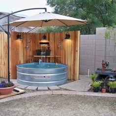 an outdoor hot tub in the middle of a yard with umbrella over it and potted plants