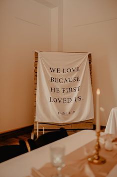 a white banner with the words we love because he first loved us on it in front of a dining room table