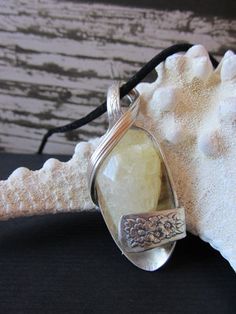 a large white stone is sitting on a black cord with a silver pendant hanging from it's end