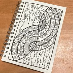 a spiral notebook with an intricate design on the cover, sitting on top of a wooden table