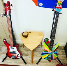 three guitars sitting on top of a wooden floor next to a table and guitar stand