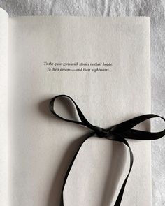 an open book with a black ribbon tied around the page and some writing on it