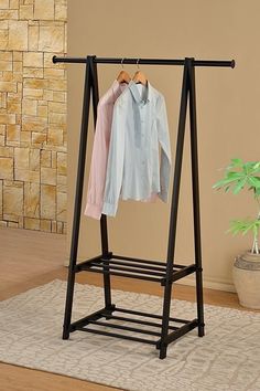 a clothes rack with two shirts hanging on it and a potted plant in the corner